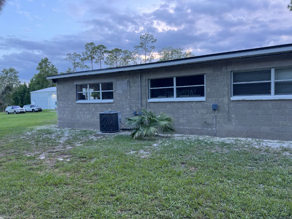 Home exterior before sandblasting — dull gray unpainted concrete block, dated and worn appearance