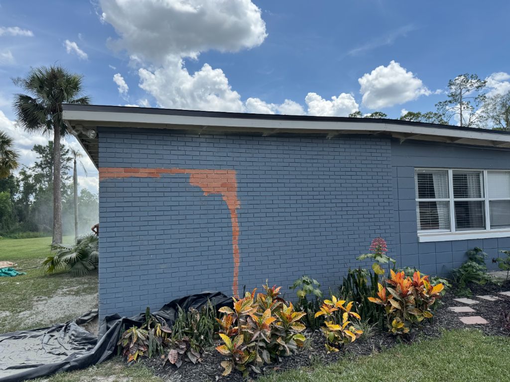 Side wall during sandblasting — gray paint being stripped to reveal vivid red brick underneath in an L-shaped pattern