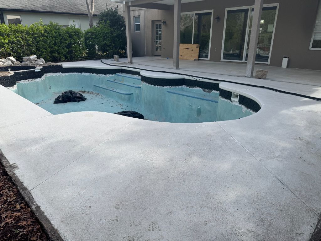 Completed pool deck epoxy removal — full surround blasted to clean bare concrete, pool drained and ready for recoat