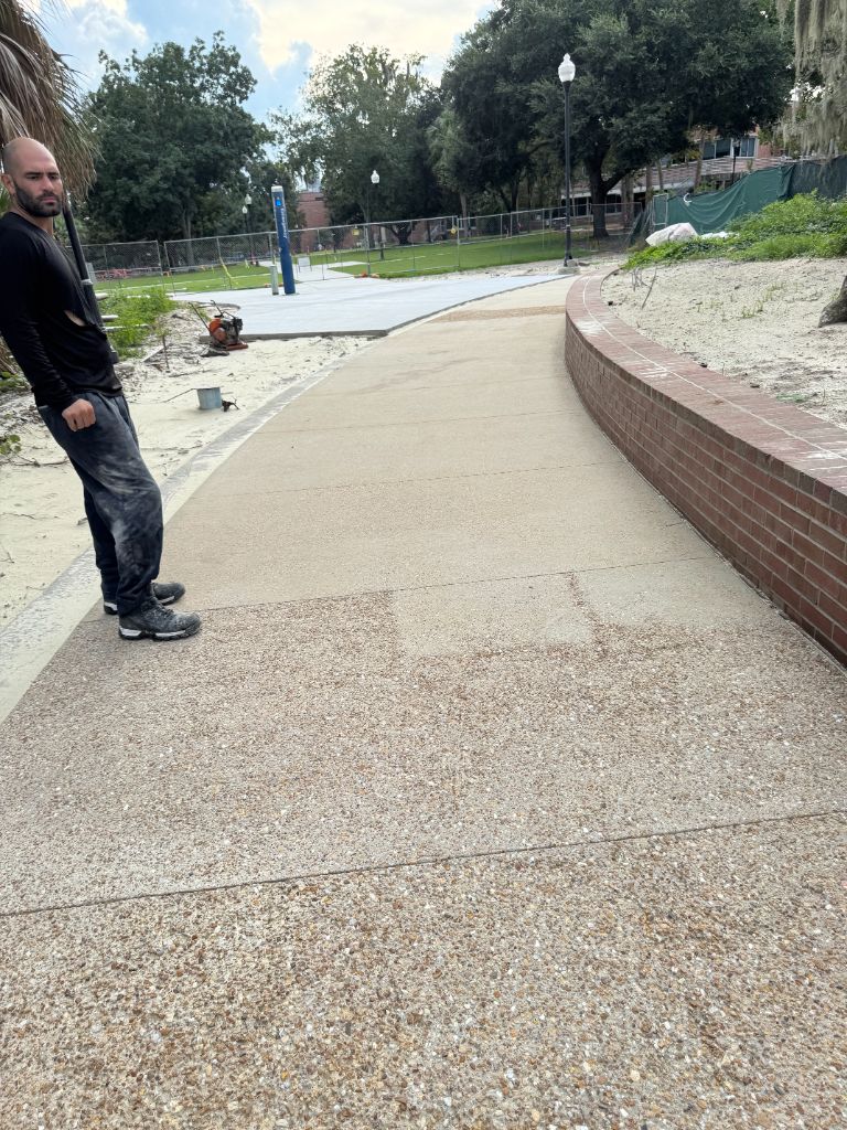UF campus sidewalk during blasting — hoses deployed, top concrete layer being stripped to expose pebble aggregate